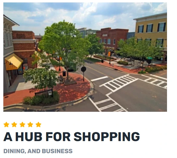 Baxter Town Center street with storefronts, trees, sidewalks, and a crosswalk, showing a walkable hub for health, fitness, offices, shopping, dining, and community services.
